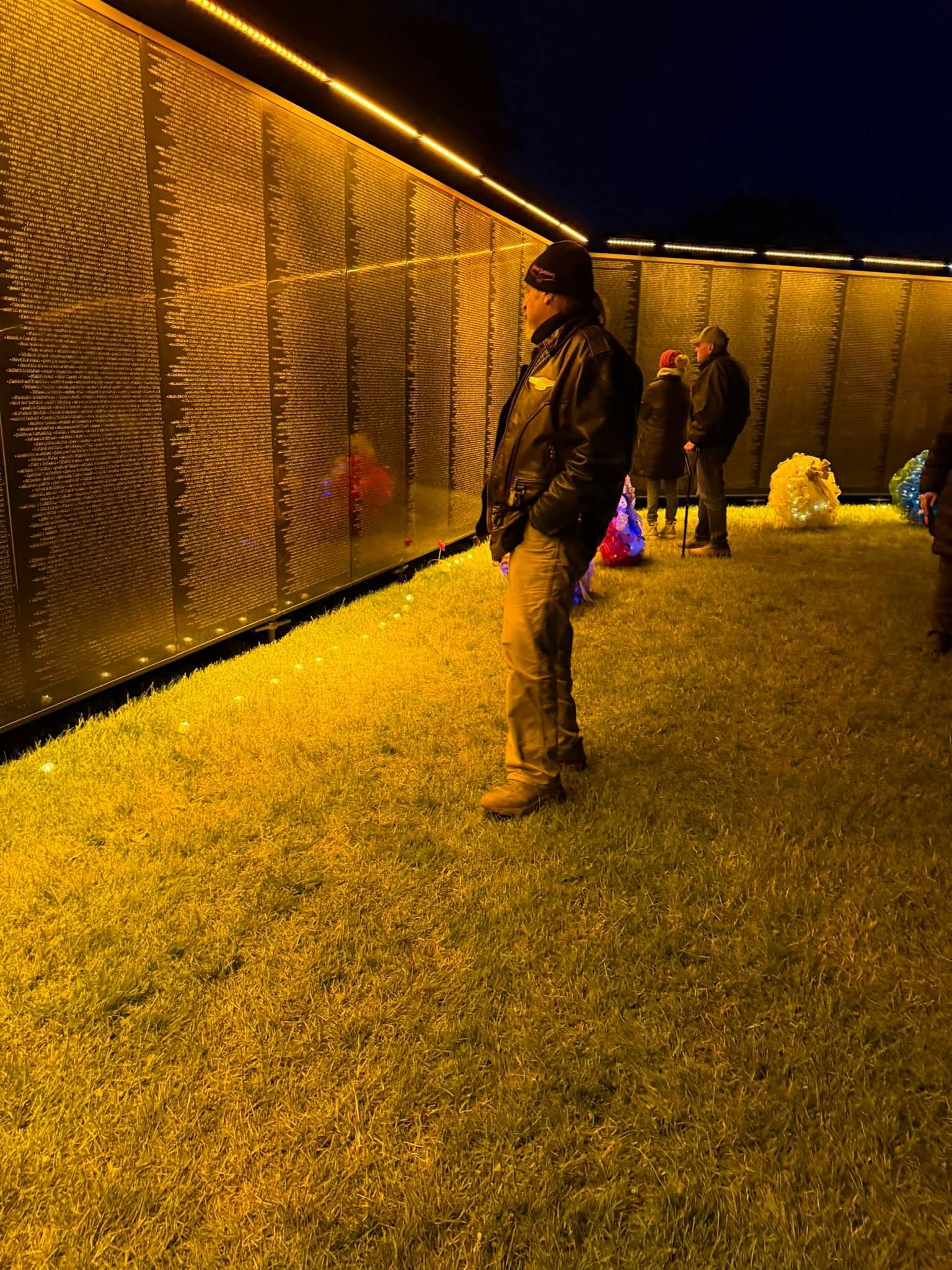 Visitors looking at the names on The Wall as it glows orange